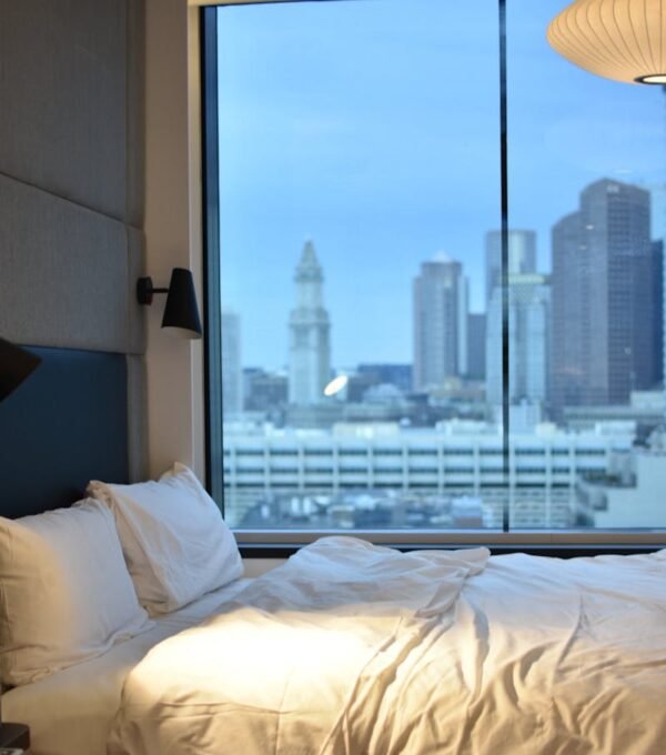 Modern hotel room overlooking Boston skyline, featuring luxury bedding.