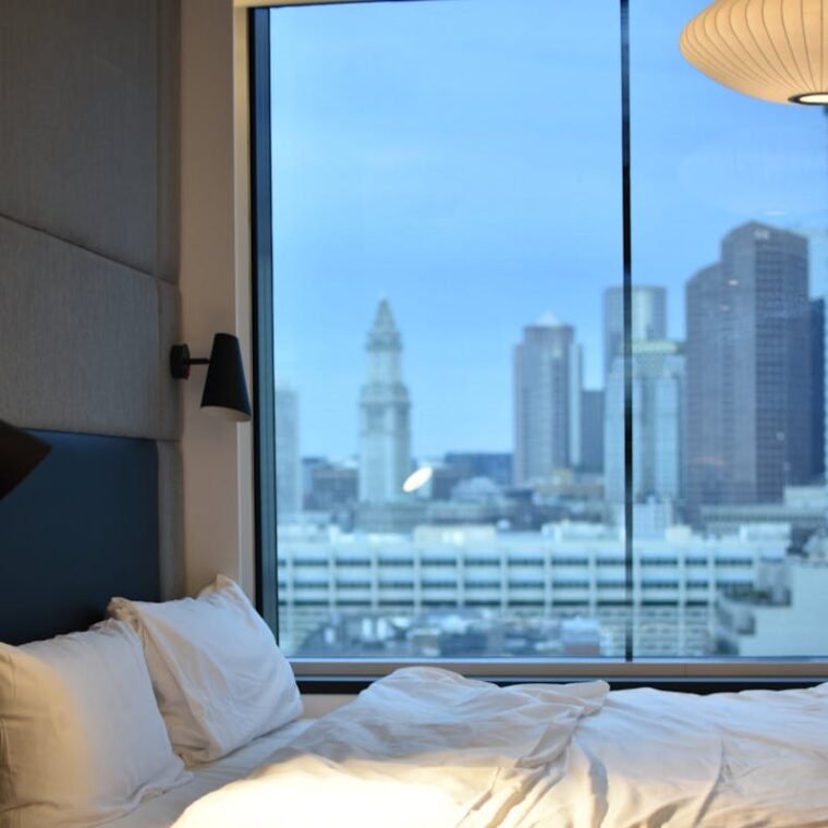 Modern hotel room overlooking Boston skyline, featuring luxury bedding.
